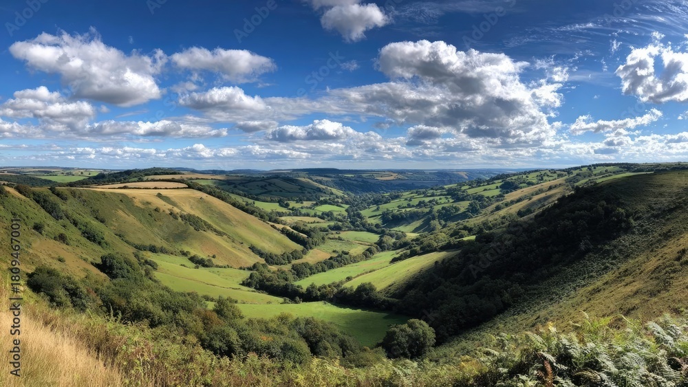 Naklejka premium Scenic countryside with rolling green hills, patchwork fields, and a blue sky dotted with white clouds. Concept Pastoral Countryside, Rolling Green Hills, Patchwork Fields, Blue Sky, Fluffy Clouds
