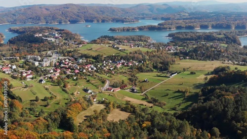 Aerial drone view of Polańczyk village and Solina Lake in Bieszczady Mountains, Poland. Scenic autumn landscape featuring rolling hills and forested shoreline.