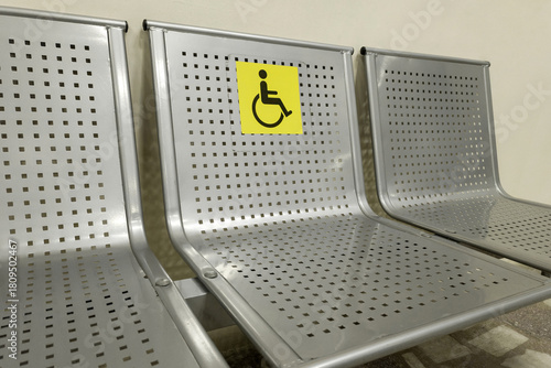 Disabled seats at the train station. Metal seats with a special yellow sign depicting a person in a wheelchair