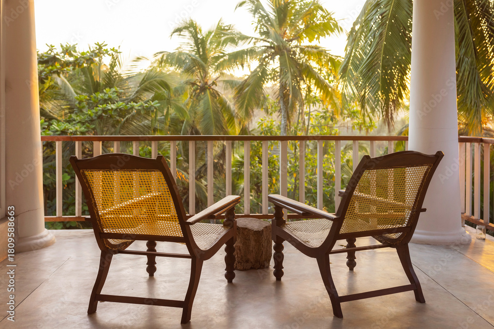 Obraz premium Tropical Resort Balcony With Two Chairs Overlooking Palm Trees At Sunset