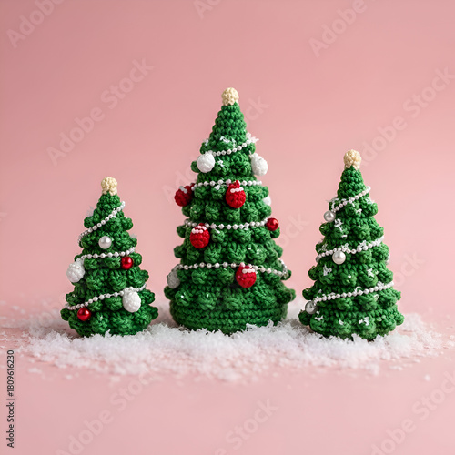 Three crocheted christmas trees with ornaments on a pink surface and snow