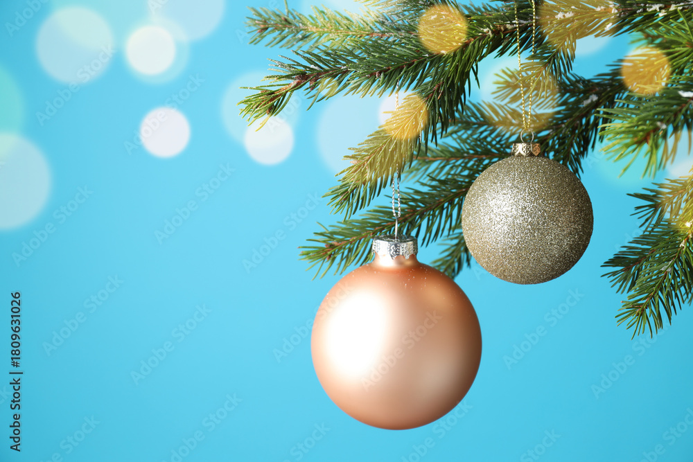 Fototapeta premium Christmas balls hanging on fir tree branches against light blue background with blurred lights, closeup with space for text. Bokeh effect
