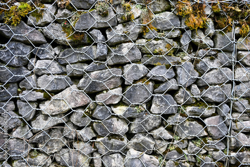 Stacked grey stones held together by a metal wire mesh, forming a sturdy gabion wall used for erosion control and landscaping
