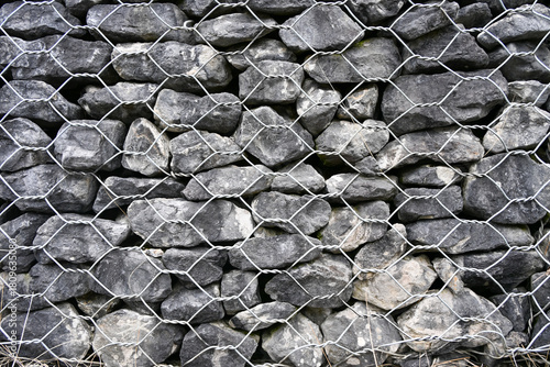 Stacked grey stones held together by a metal wire mesh, forming a sturdy gabion wall used for erosion control and landscaping