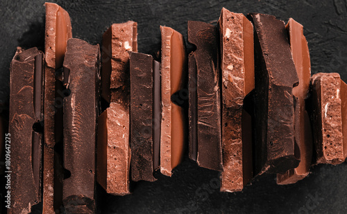 Assorted stacked chocolate bar pieces with rich textures and broken edges on dark background for premium confectionery branding and dessert advertising