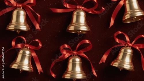 Golden bells with red ribbons arranged on a dark, textured surface, creating a festive aesthetic