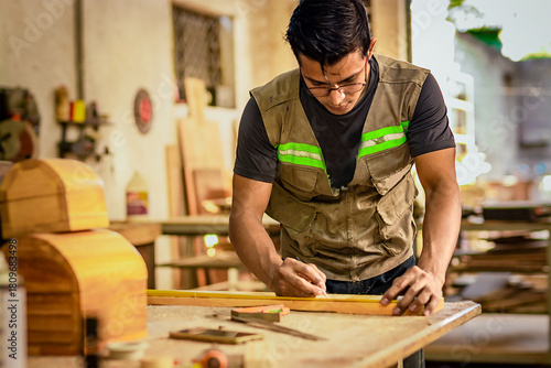 Carpenter with glasses taking measurements at the workbench. Young cabinetmaker measuring a piece with a tape measure in the workshop