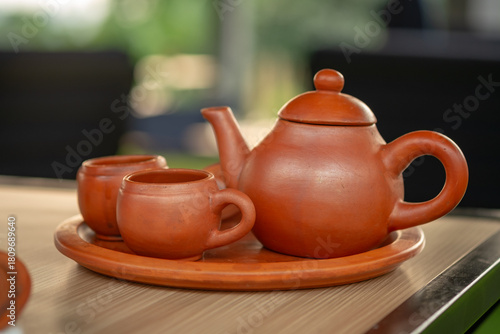 Traditional clay teapot and cups (Teh Poci) from Central Java on a tray. A rustic earthenware tea set, typical of Tegal culture, serving hot tea against a blurred background.