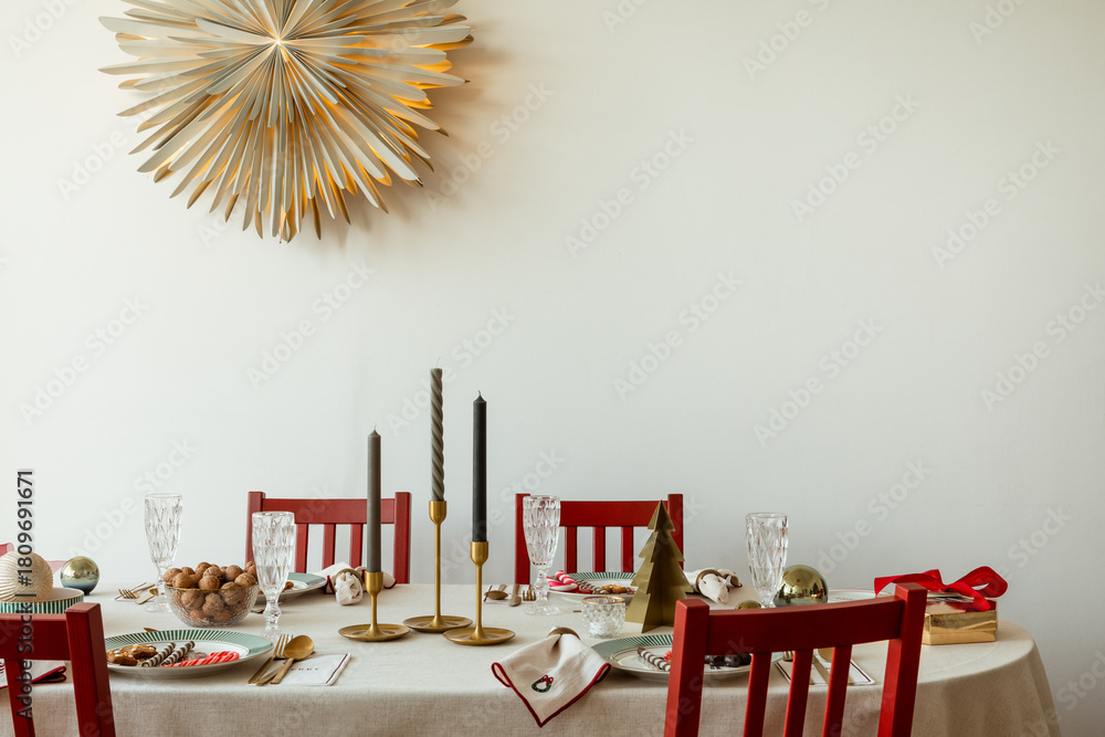 Obraz premium Elegant Christmas table setting with gold candle holders, crystal glasses, festive plates, and subtle holiday details.