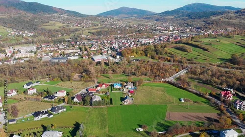 Aerial view of Mszana Dolna town center nestled in the Beskidy Mountains, Poland. Scenic autumn panorama featuring residential areas, river, and forested rolling hills.