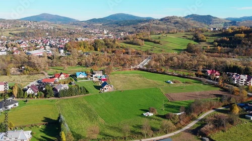 Aerial view of Mszana Dolna town center nestled in the Beskidy Mountains, Poland. Scenic autumn panorama featuring residential areas, river, and forested rolling hills.