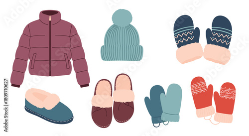 A cozy collection of warm winter clothes and accessories including a puffer jacket hat mittens and slippers on white.