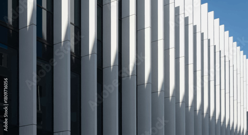 Modern architectural facade featuring vertical white and gray panels creating striking shadows.