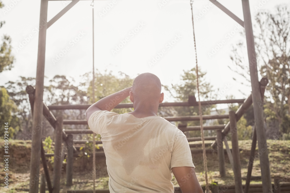 Obraz premium Man standing centered at park, facing wooden obstacle structure with ropes and damp sweat on shirt