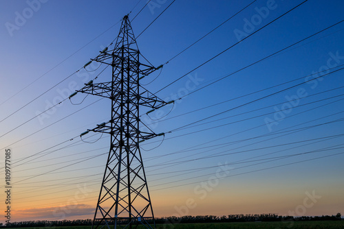A tall power tower with many wires is silhouetted against a blue sky