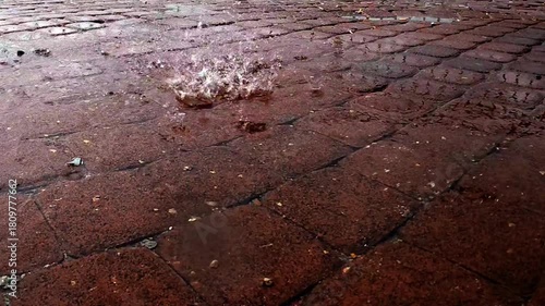 Slow motion rain falling on pavement tiles, close-up shot with water drops splashing