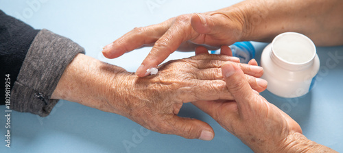 Woman applying cream to elderly female hands.