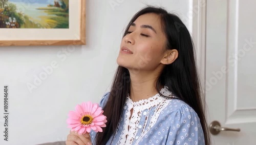 Beautiful Asian Woman Enjoying the Scent of a Pink Gerbera Daisy Indoors.