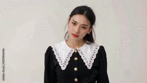 Beautiful Young Asian Woman in Black Dress with White Collar Posing and Smiling on White Background.