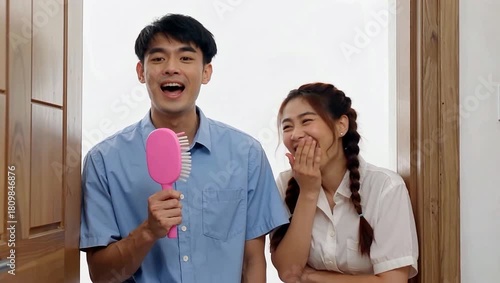 Young Asian couples playful surprise and laughter with a pink hairbrush.