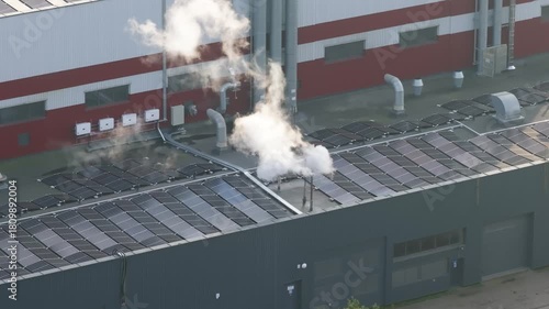 Vapor smoke coming from industrial factory site, roof covered with solar panels, aerial view