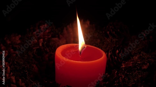 Candle flame flickers gently in a dark room surrounded by pinecones and nature