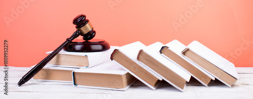 Law concept - Open law book, Judge's gavel, scales, Themis statue on table in a courtroom or law enforcement office. Wooden table, orange background.