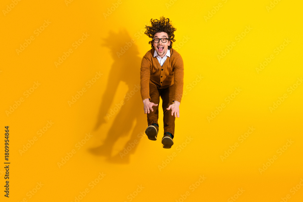 Naklejka premium Young man jumping in mid air wearing cardigan and glasses against bright yellow background smiling and having fun