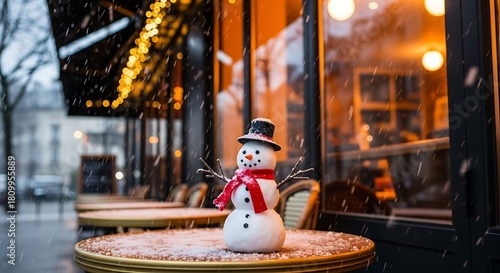 Fototapeta Naklejka Na Ścianę i Meble -  Small snowman with black hat and red scarf on cafe table in falling snow winter