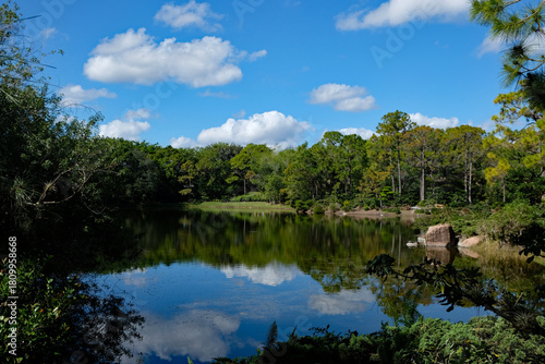 Looking across a lake with a blue sky and clouds reflected with rock boulders along the shoreline
