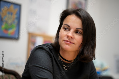 a beautiful dark-haired woman sitting at a desk in an office, looking to the side with a blurred background. Professional business scene