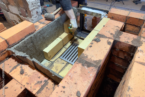 Formation of a fireclay core for a solid fuel furnace. A bricklayer is laying fireclay bricks. Cast iron grate has been installed. Construction of a heating furnace.