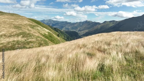 Aerial view of a wide mountain valley featuring yellow dry grasslands in the foreground and majestic peaks in the distance on a sunny autumn day in Gudauri, Georgia