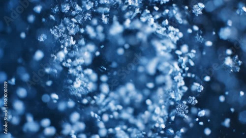 A close-up of ice crystals and snowflakes drifting against a dark blue background, with crisp edges, soft bokeh, and shallow focus for a tranquil winter scene. Snow swirl