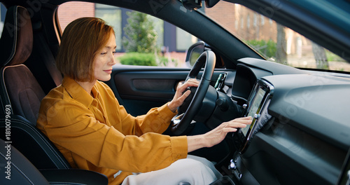 Beautiful young woman setting up navigation on a screen inside a modern car, preparing for a road trip. Concept of technology, travel, connectivity, and contemporary lifestyle
