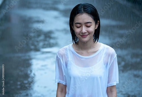 Happy young Asian woman with eyes closed enjoying the rain. Portrait of a person getting soaked in a downpour. Concept of relief and mindfulness