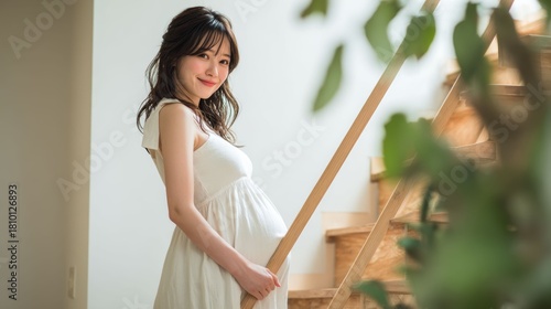 観葉植物越しに見る白いワンピースの妊婦のナチュラルな写真