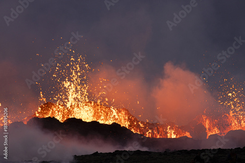 View of molten lava erupting in a volcanic display, contrasting against the dark sky with billowing smoke, in a moment of geological drama, Reykjanes, Grindavíkurbaer, Iceland.