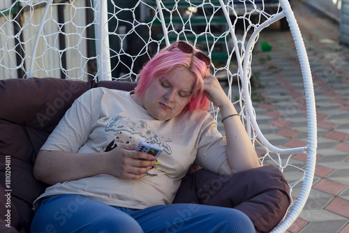 a girl with pink hair is sitting in a chair, reading messages on her phone