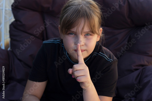 a teenage girl sitting in a chair, her finger pressed to her lips, keeping a secret.