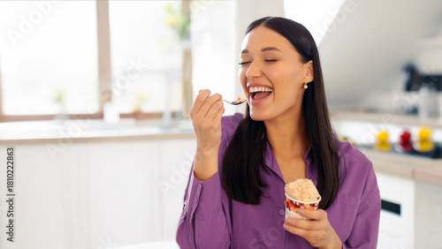 Attractive woman with tasty ice cream in kitchen, lady enjoy having cheat meal time and eating sweet dessert, space for text