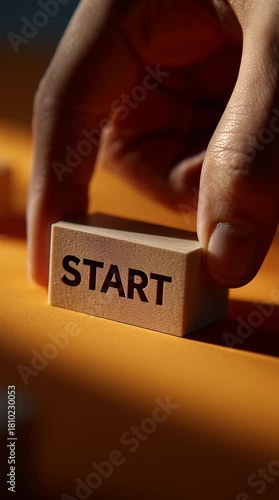 Hand pushing wooden block labeled start on orange surface close up, symbolizing motivation, business concept, and decision in warm light setting