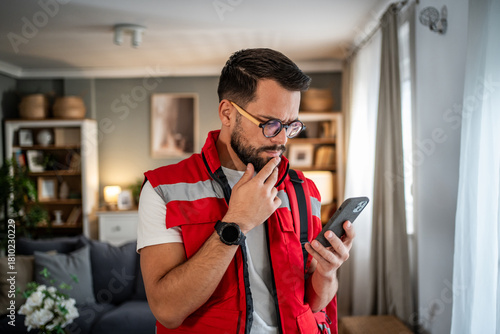 Thoughtful paramedic man using smart phone at home