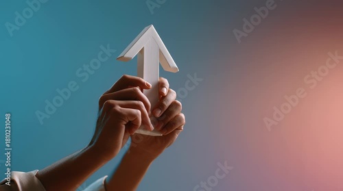 Hands holding white arrow prop pointing upward with soft gradient background symbolizing growth progress direction and positive symbol of success