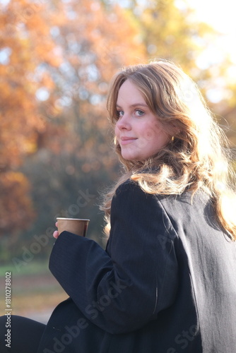 Canvastavla Girl is sitting on a bench in city autumn park with paper cup of coffee
