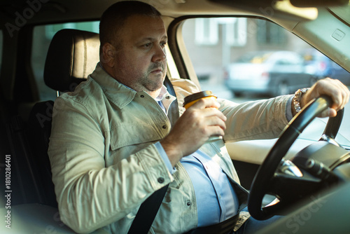 Mature man driving with coffee in city traffic, tired