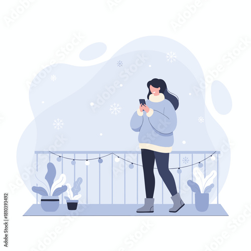 Cozy woman uses phone on a snowy balcony with festive lights Winter leisure and communication