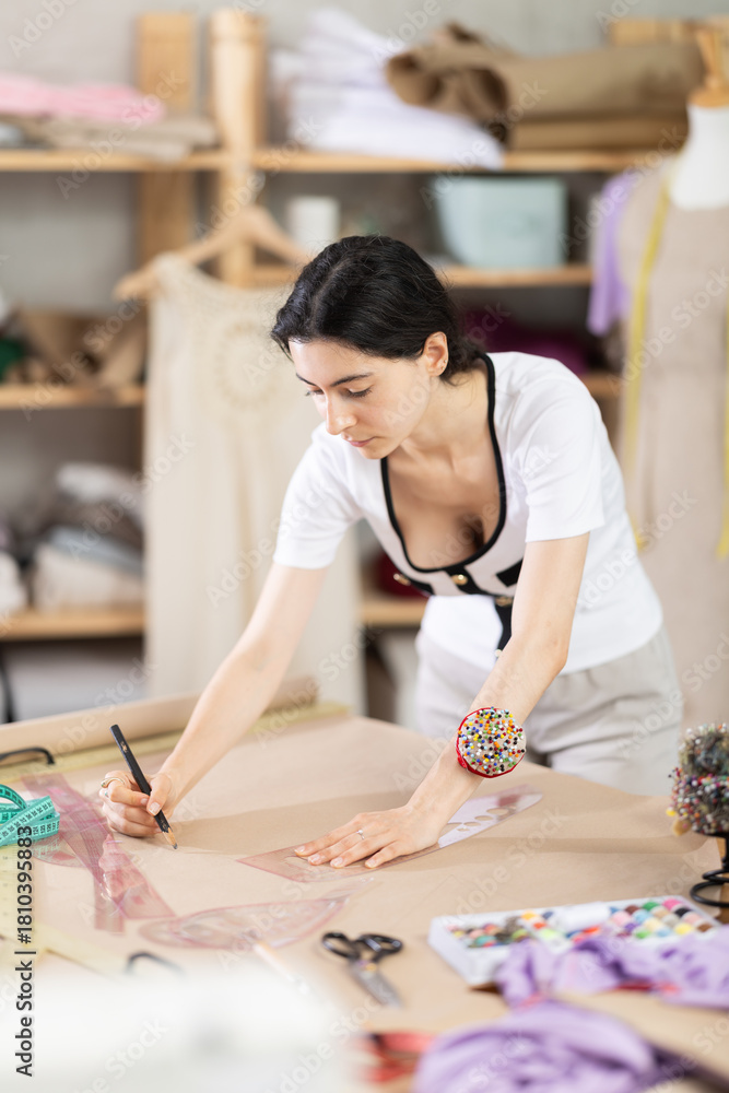 Fototapeta premium Armenian woman works as a fashion designer in a sewing workshop and draws patterns for clothes using curved rulers