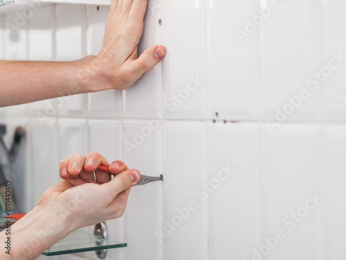 A young man pulls out a dowel from the wall using pliers.