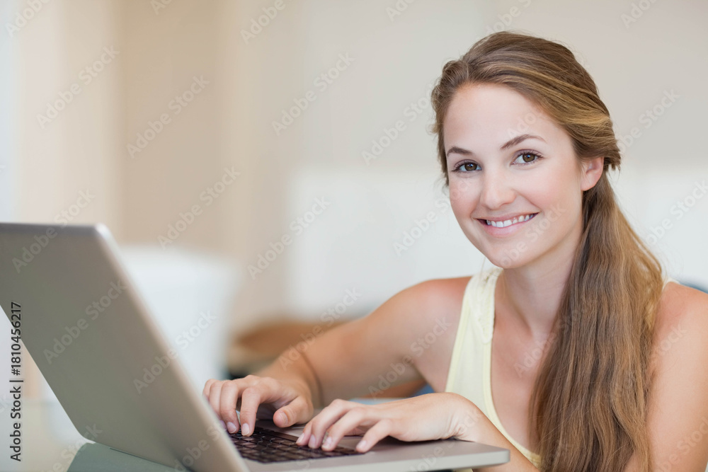Fototapeta premium Woman sitting at table typing on laptop keyboard with hands resting in bright softly lit room